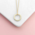 Gold necklace with a circular pendant on a white and pink gradient background