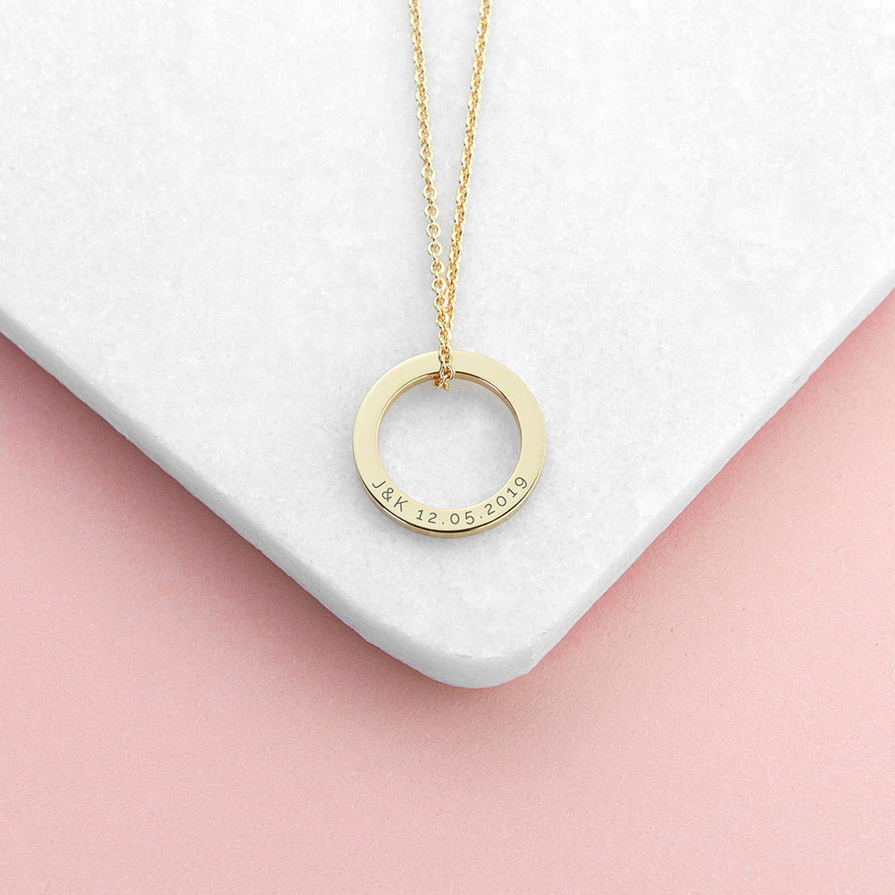 Gold necklace with a circular pendant on a white and pink gradient background