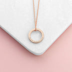 Rose gold necklace with a circular pendant on a white and pink gradient background