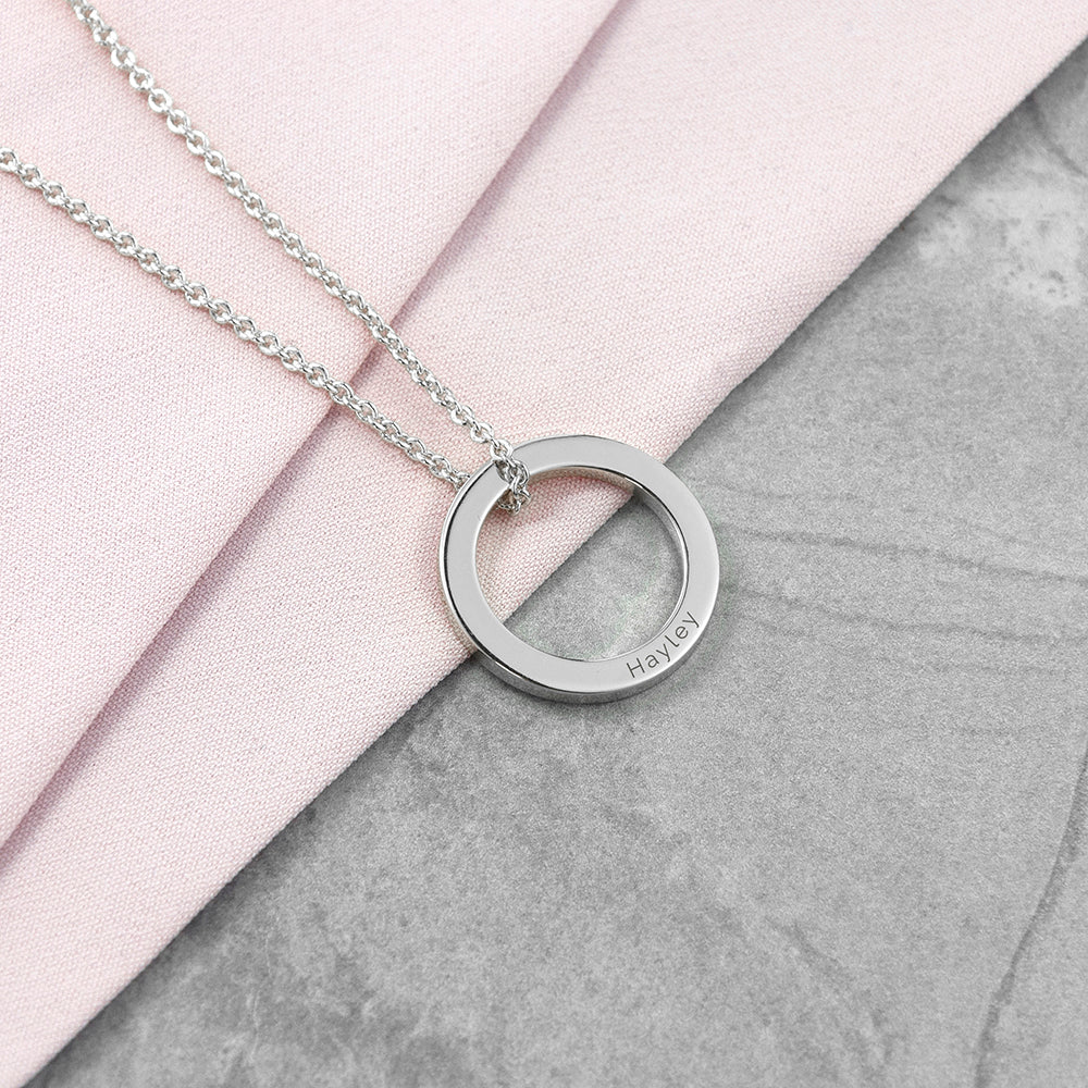 Silver necklace with a circular pendant on a pink and gray surface