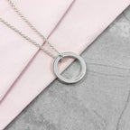 Silver necklace with a circular pendant on a pink and gray surface