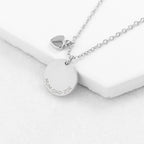 Silver necklace with a round pendant engraved with 'Julia' on a white surface
