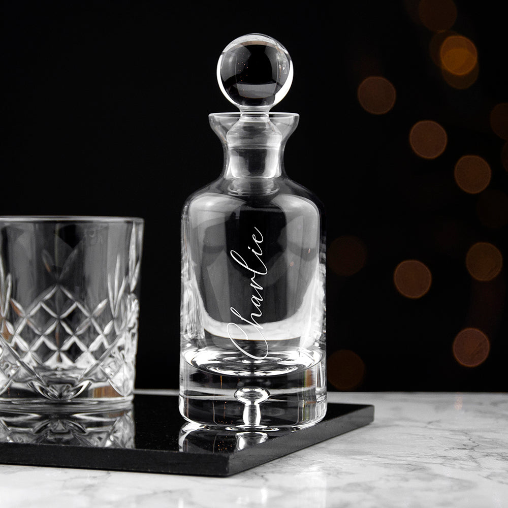 Clear glass decanter with 'Charlie' engraving on a black tray with a blurred background