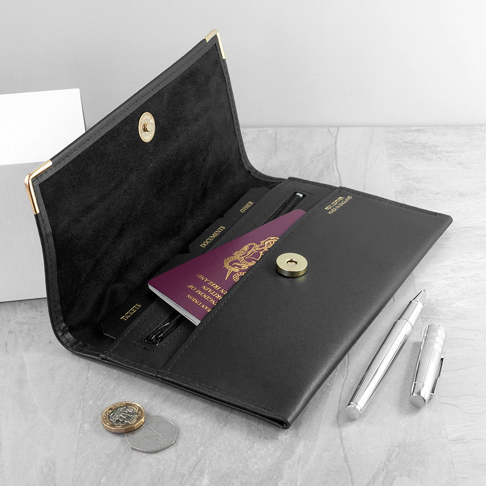 Black leather travel wallet with passport, pen, and coins on a light gray surface