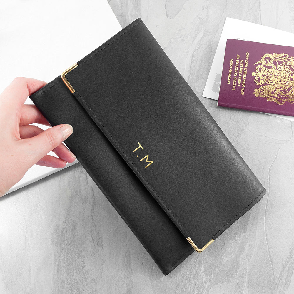 Black passport holder with gold initials next to a purple passport on a light gray surface