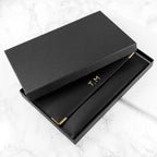 Black box with gold 'T.M' initials on a white marble surface