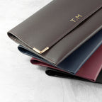 Three leather wallets in different colors stacked on a light gray surface with 'T.M' branding.