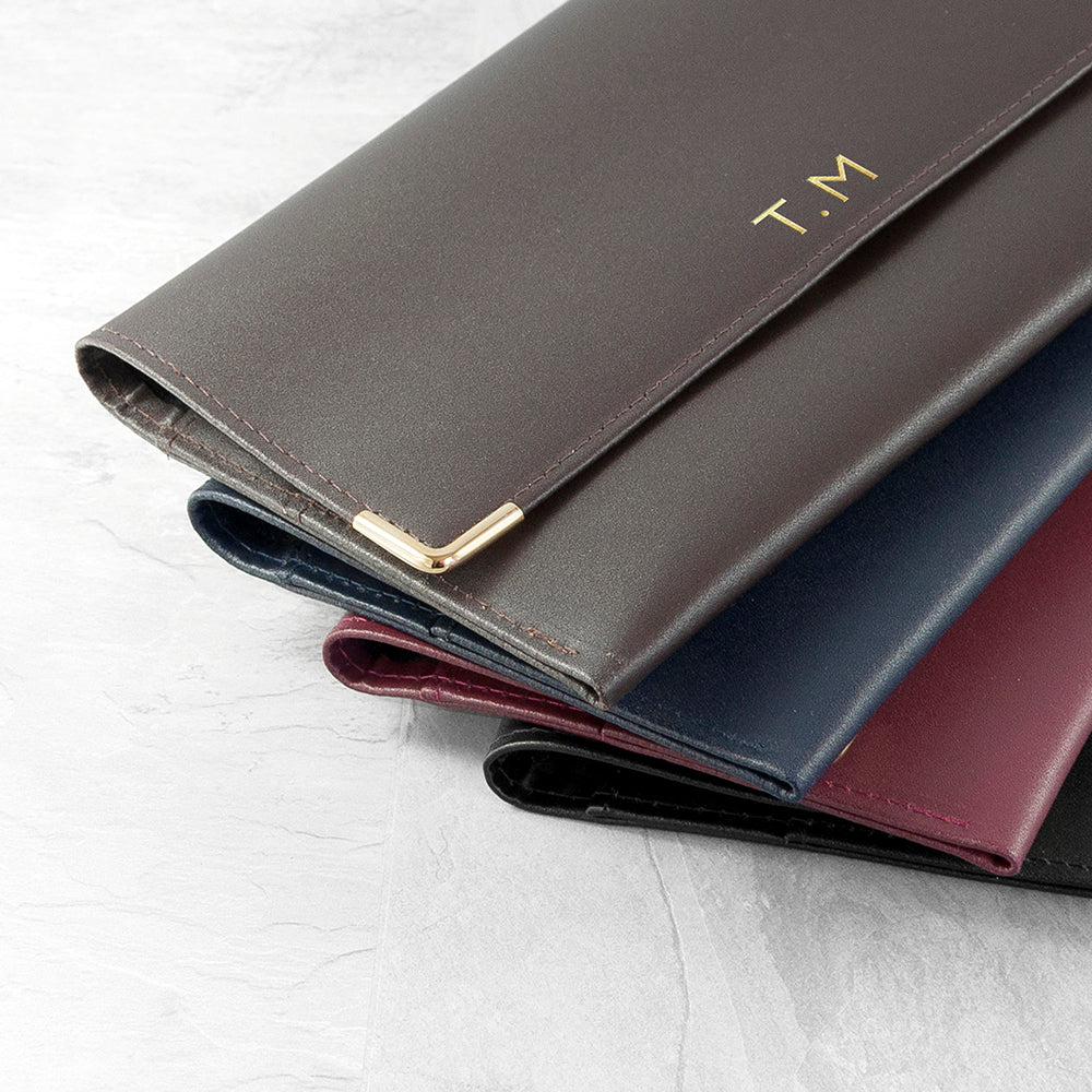 Three leather wallets in different colors stacked on a light gray surface with 'T.M' branding.
