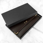 Black box with gold 'T.M' initials on a white marble surface