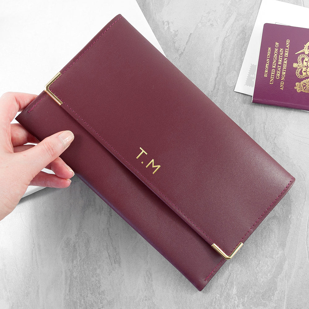 Maroon travel wallet with gold monogram on a light gray surface with a passport.