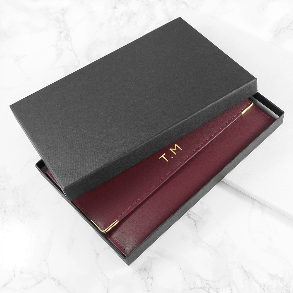 Maroon wallet with gold accents in a black box on a white background