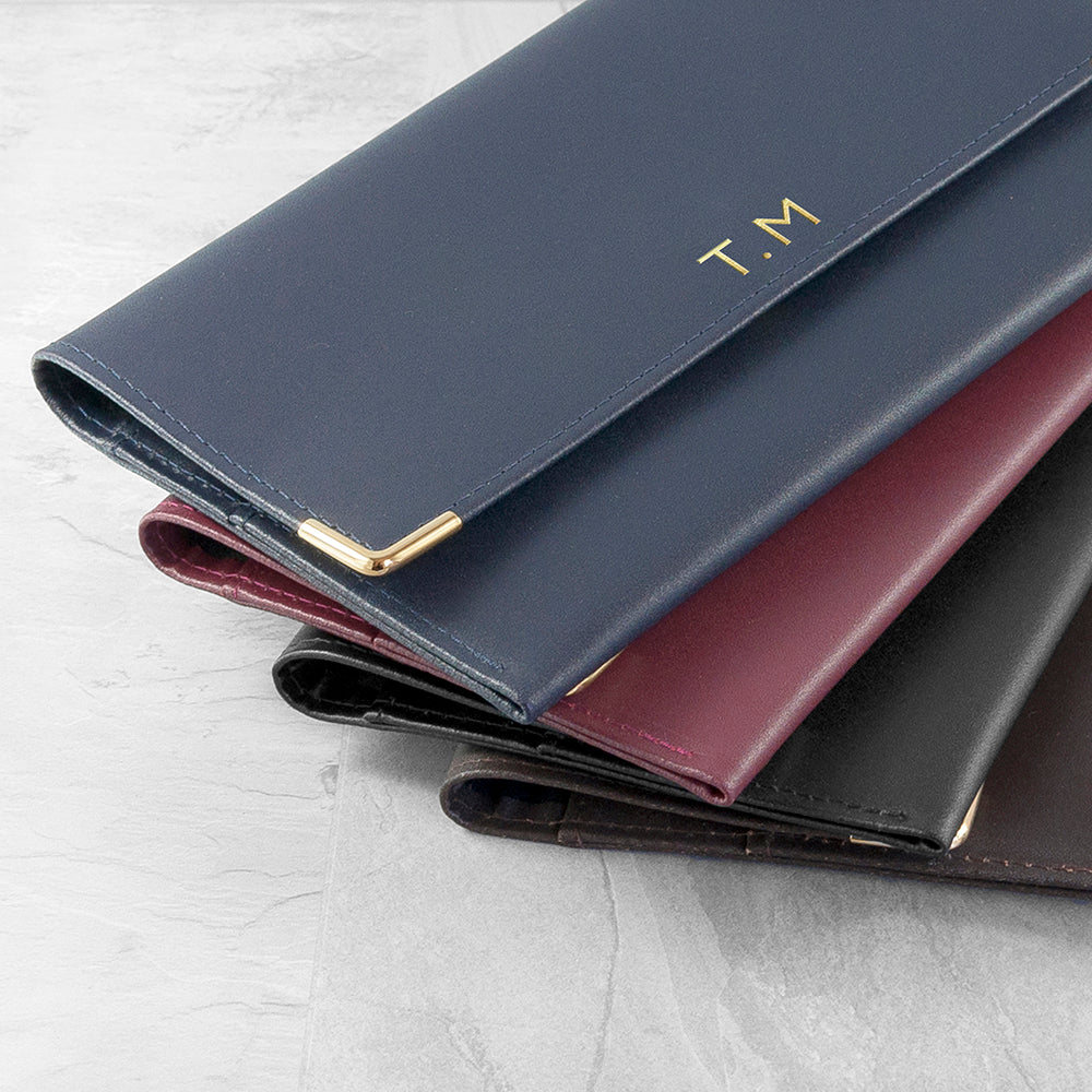 Three leather wallets in different colors stacked on a light gray surface with 'T.M.' branding.