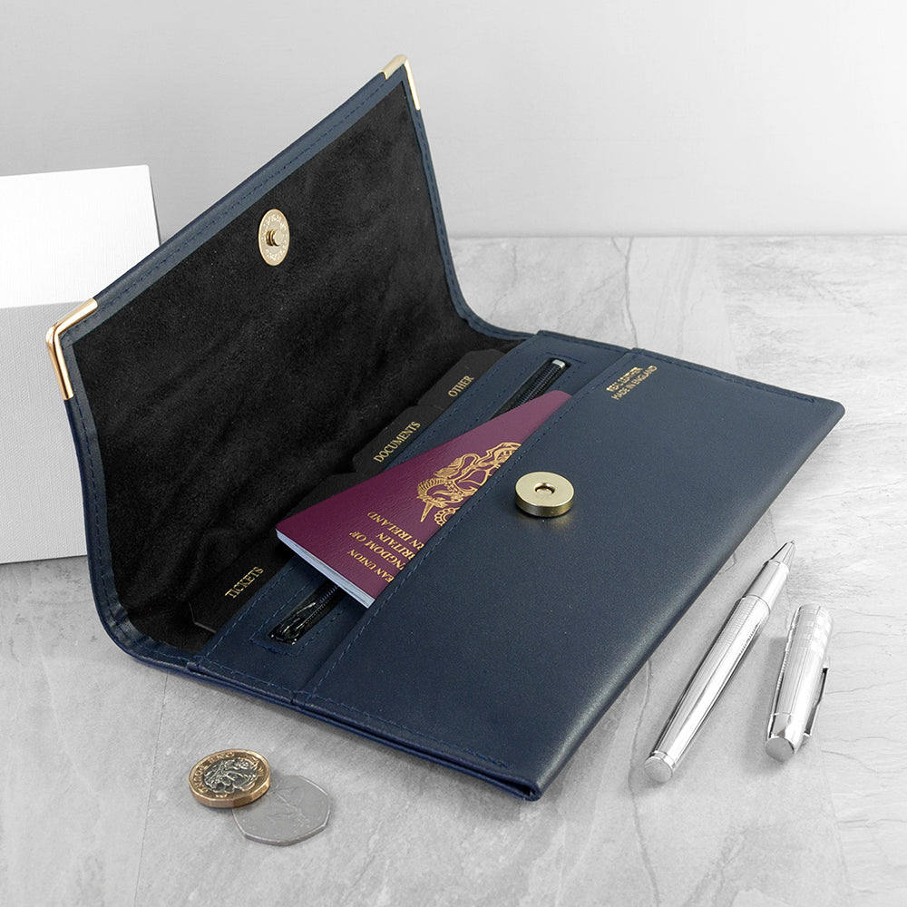 Navy leather travel wallet with passport, pen, and coins on a light gray surface