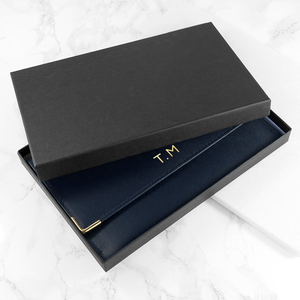 Black leather clutch with gold accents inside an open black box on a white marble surface