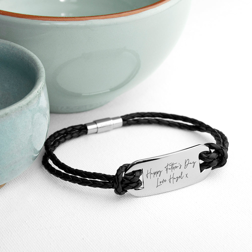 Black braided bracelet with a silver tag on a white surface with ceramic bowls in the background