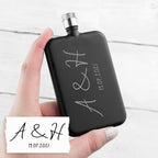 Black flask held by a hand with 'A & H' and date engraved on it, against a white background.