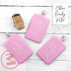 Three pink flasks with names engraved on them, placed on a wooden surface.