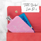 Pink hand warmer with 'Total Babe' text inside a red wallet on a marble background