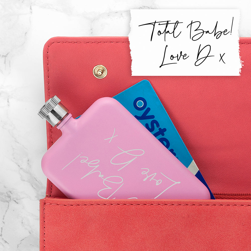 Pink hand warmer with 'Total Babe' text inside a red wallet on a marble background