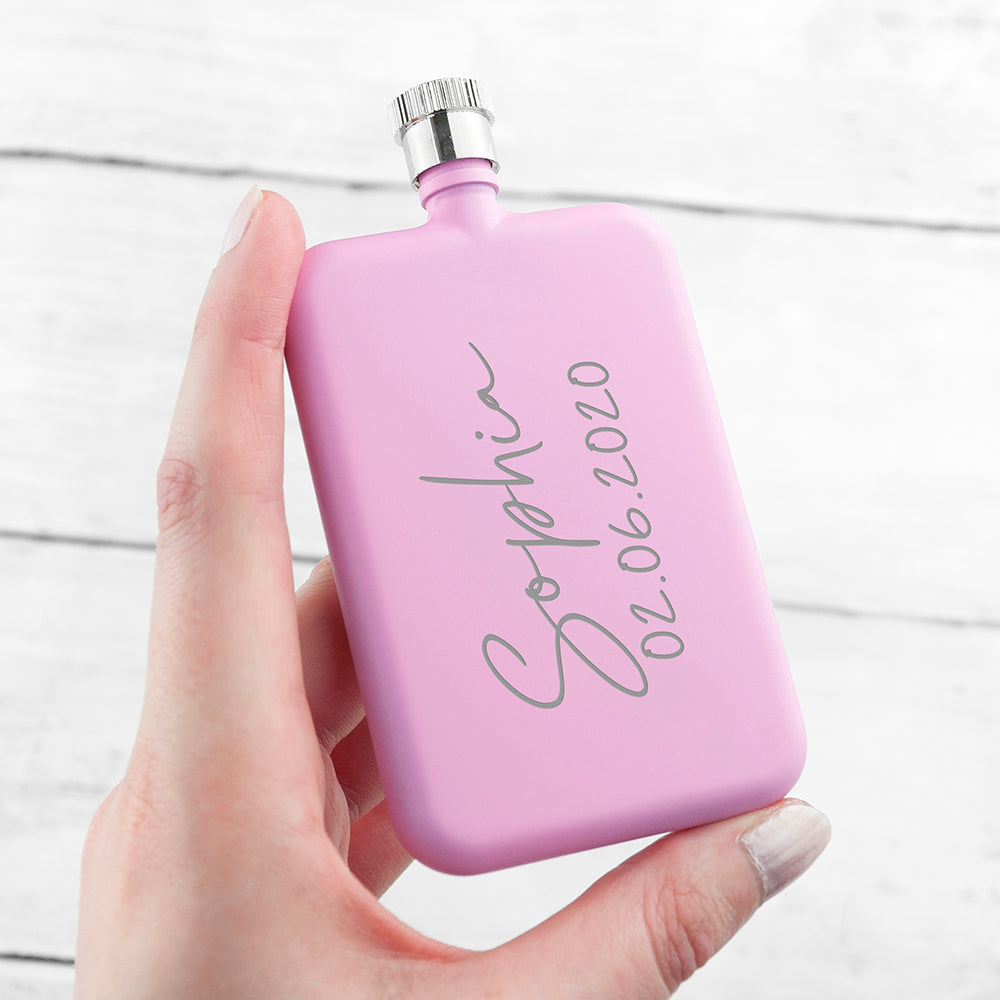 Hand holding a pink flask with engraved text on a white background