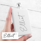 White flask with 'Elliot' branding held by a hand on a light background