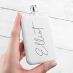 White flask with 'Elliot' branding held by a hand on a light background