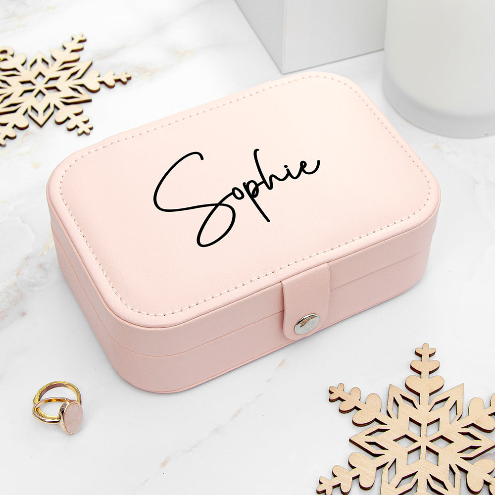 Pink jewelry box with 'Sophie' engraving on a white surface with wooden snowflakes.