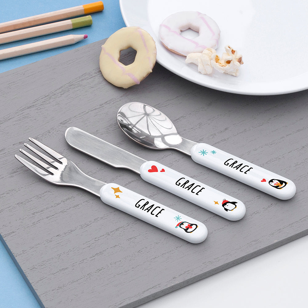 Children's cutlery set with personalized handles on a gray surface, surrounded by snacks.