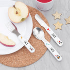 Children's cutlery set with 'JACK' on a plate with apple slices and a cup.