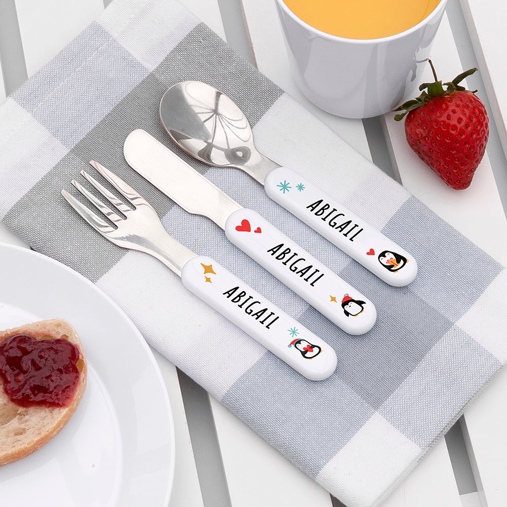 Personalized cutlery set with 'ABIGAIL' on a checkered tablecloth with a strawberry and cup of tea.