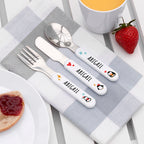 Personalized cutlery set with 'ABIGAIL' on a checkered tablecloth with a strawberry and cup of tea.