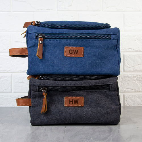 Two blue toiletry bags with brown leather tags stacked on a white brick wall background
