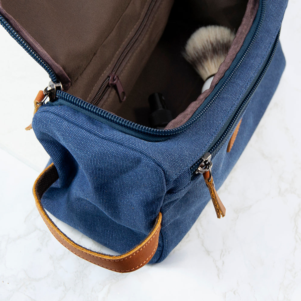 Blue toiletry bag with brown leather accents on a white background