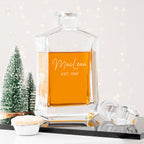 Glass decanter with brand name and establishment year on a reflective surface with decorative elements.
