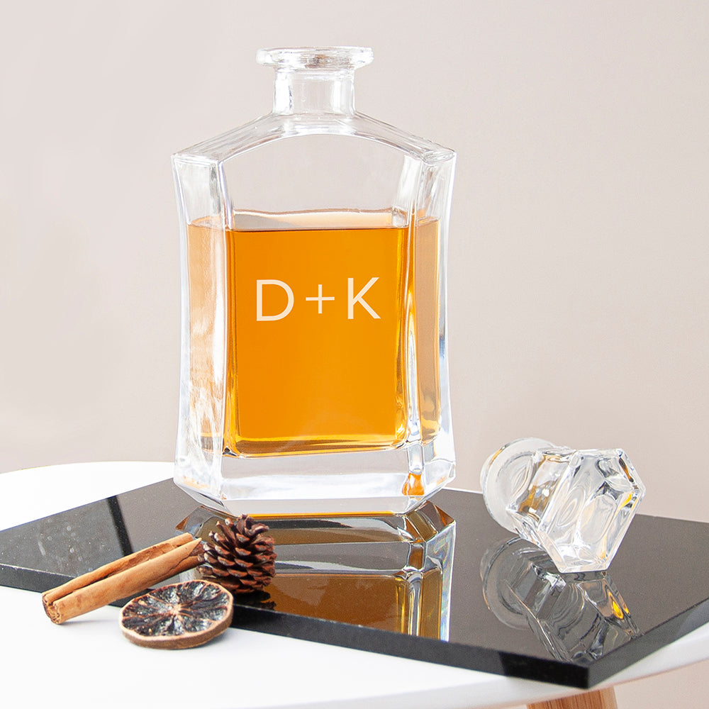 Clear glass decanter with amber liquid on a reflective surface, with 'D+K' initials.
