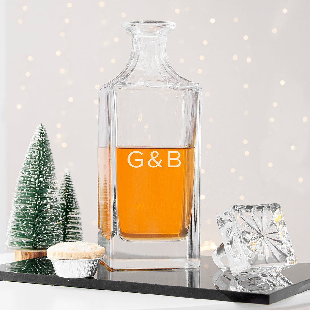 Clear glass decanter with brand name and establishment year, filled with amber liquid, on a decorative surface.