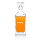 Clear glass decanter with orange liquid and 'WPF' initials on a white background