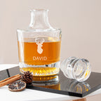 Personalized glass decanter with brandy, branded 'DAVID', on a reflective surface.