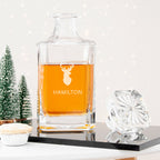 Clear glass decanter with orange liquid and engraved 'G' and 'GIBSON' on a white surface.