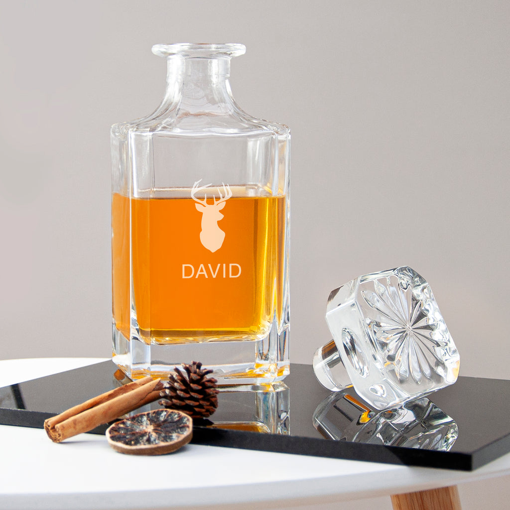 Clear glass decanter with amber liquid, branded 'DAVID', on a table with decorative items.