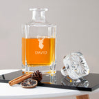 Clear glass decanter with amber liquid, branded 'DAVID', on a table with decorative items.