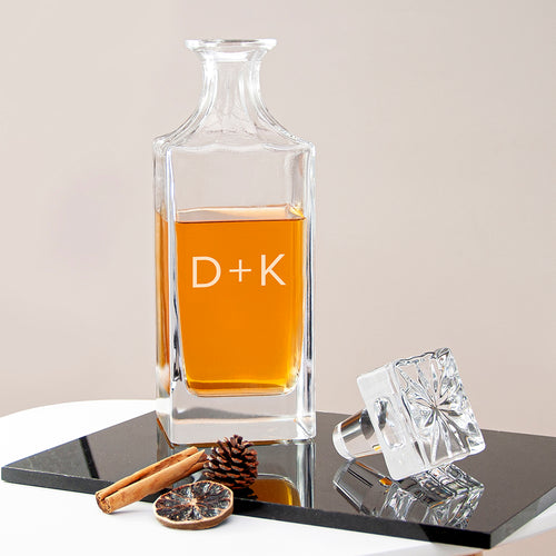 Clear glass decanter with amber liquid on a reflective surface with decorative items.