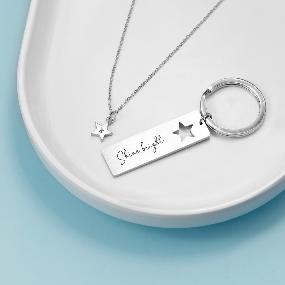 Silver necklace and keychain set on a white dish with a light blue background