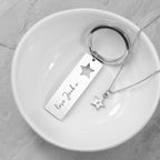 Silver keychain and necklace with star pendants on a white dish.