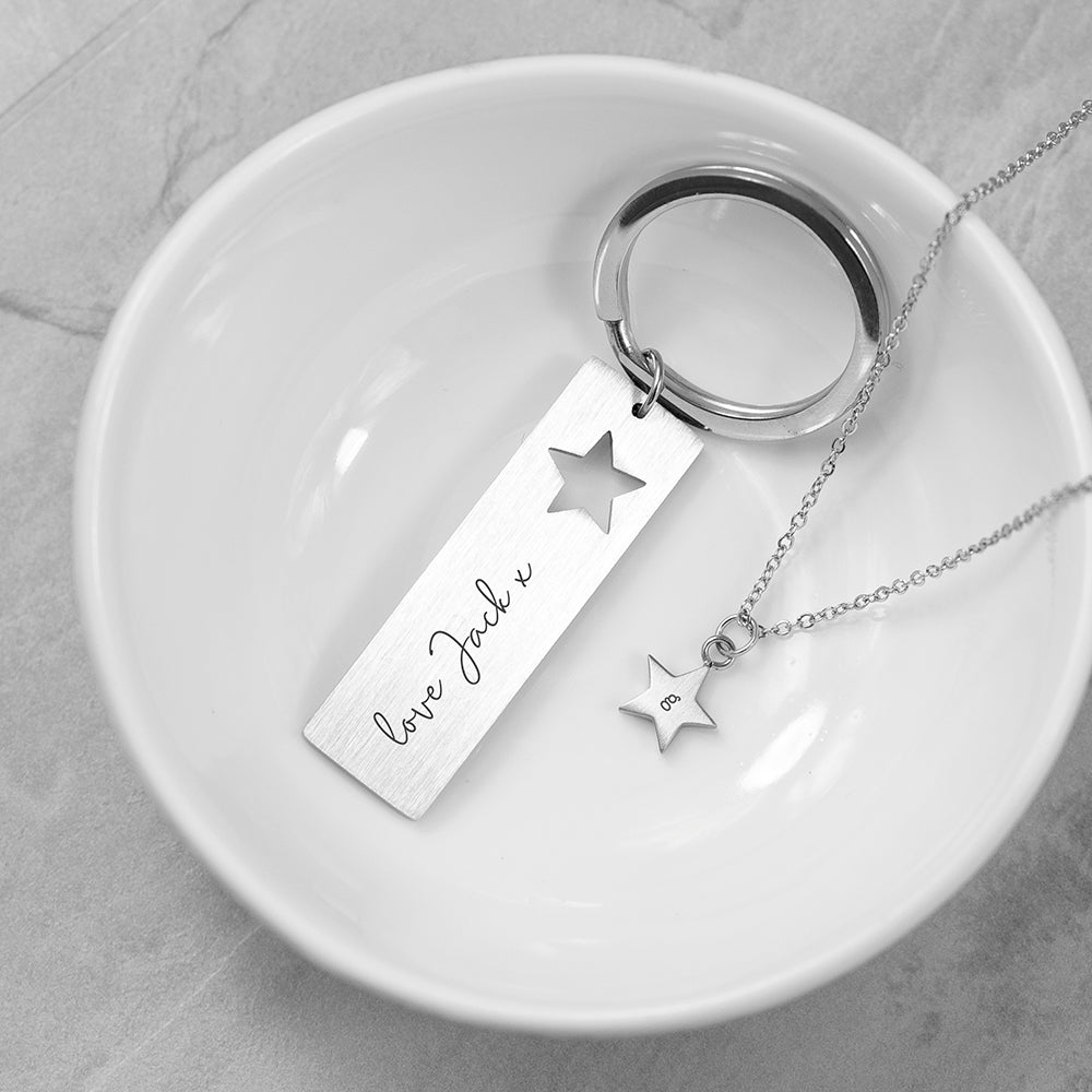 Silver keychain and necklace with star pendants on a white dish.