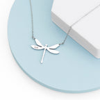 Silver dragonfly necklace on a light blue surface with a white box in the background