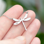 Silver dragonfly necklace held in a hand with a blurred green background
