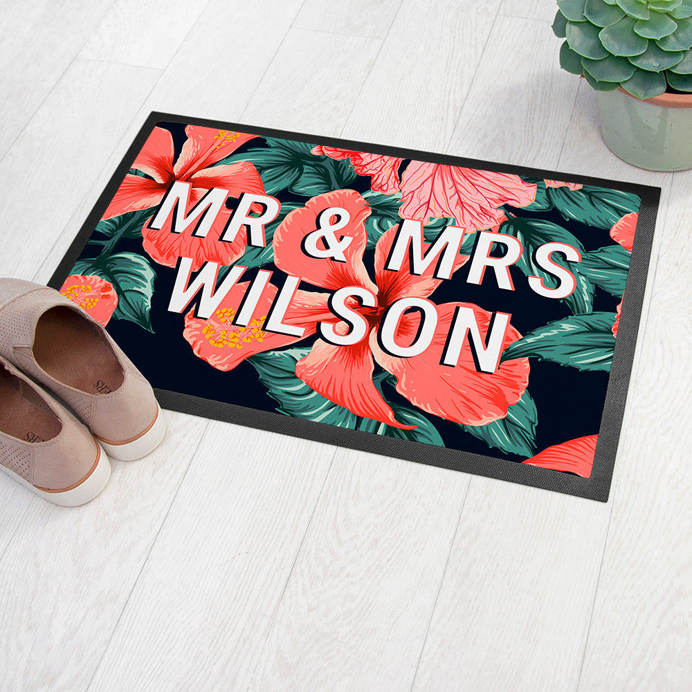 Floral doormat with 'MR & MRS WILSON' text on a white floor with shoes and a plant.