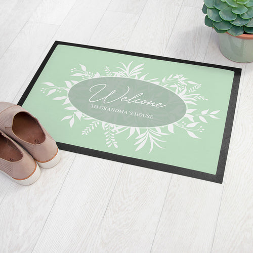 Doormat with 'Welcome to Grandma's House' text on a light wooden floor.