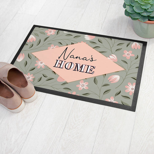 Decorative doormat with floral pattern and 'Nana's Home' text on a light wooden floor.